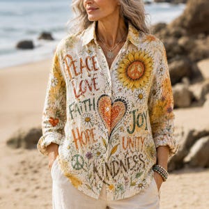 Puede incluir: Una camisa de manga larga con botones sobre un fondo crema con un estampado de girasoles y flores silvestres. La camisa muestra las palabras Peace, Love, Faith, Hope, Joy, Unity y Kindness, junto a un gran corazón central y símbolos de paz.