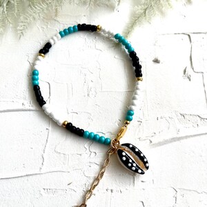 May include: A white, black, and turquoise beaded bracelet with a gold chain and a black and white seashell charm.