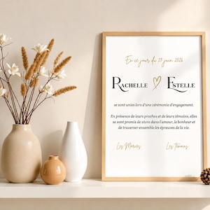 Peut inclure: Une affiche verticale encadrée avec le texte noir Rachelle et Estelle, séparé par un cœur doré, et du texte français en dessous. L'affiche est présentée à côté d'un vase beige avec des fleurs séchées, un petit vase blanc et une pomme de pin.