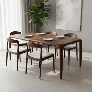 May include: A rectangular dark wood dining table with rounded corners and four matching chairs. Each chair features a curved backrest and a white upholstered seat. Four white plates are arranged on the table surface, which has a smooth finish.