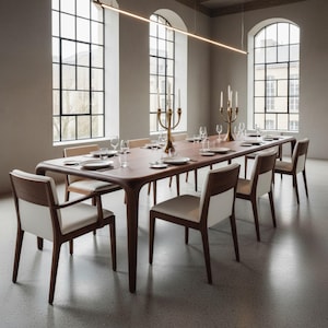 May include: A long, dark wood dining table with rounded edges and tapered legs, surrounded by eight chairs featuring dark wood frames and white upholstered seats. Two brass candelabras with white candles sit on the table with glassware.