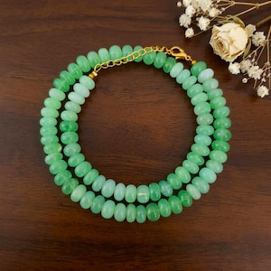 May include: A necklace composed of numerous round, translucent light green beads strung together. The piece features a gold-toned metal chain section with a lobster claw clasp, allowing for adjustable length. The beads have a smooth, polished finish.