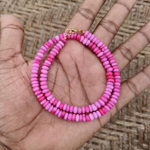 May include: A necklace composed of small, round, vibrant pink beads strung together in a circular pattern. The necklace features a gold-toned metal lobster claw clasp at the top, connecting the two ends of the beaded strand securely.