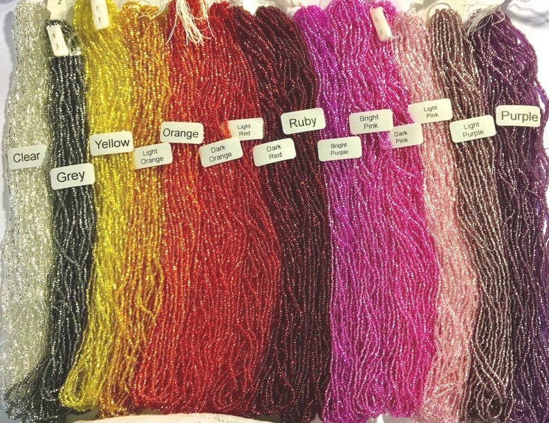 Puede incluir: Surtido de cuentas de semillas en varios colores, incluyendo transparente, gris, amarillo, naranja, rojo, rub&iacute;, morado, rosa y rosa claro. Las cuentas est&aacute;n dispuestas en filas por color.
