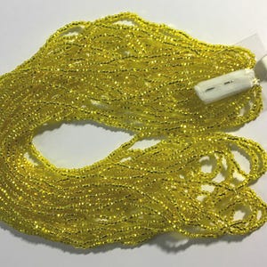 Puede incluir: Un gran carrete de cuentas de semillas de color amarillo brillante con un borde plateado. Las cuentas est&aacute;n dispuestas en una pila suelta, con algunas hebras superpuestas. La etiqueta dice "Silver lined Yellow".