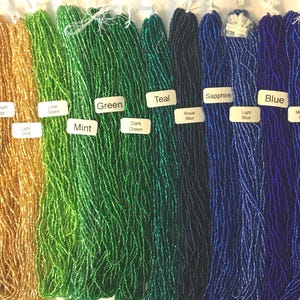 Puede incluir: Una variedad de cuentas de semillas en diferentes colores, incluyendo marr&oacute;n, dorado, verde, azul verdoso, zafiro, azul y azul marino. Las cuentas est&aacute;n dispuestas en filas, con cada fila representando un color diferente.