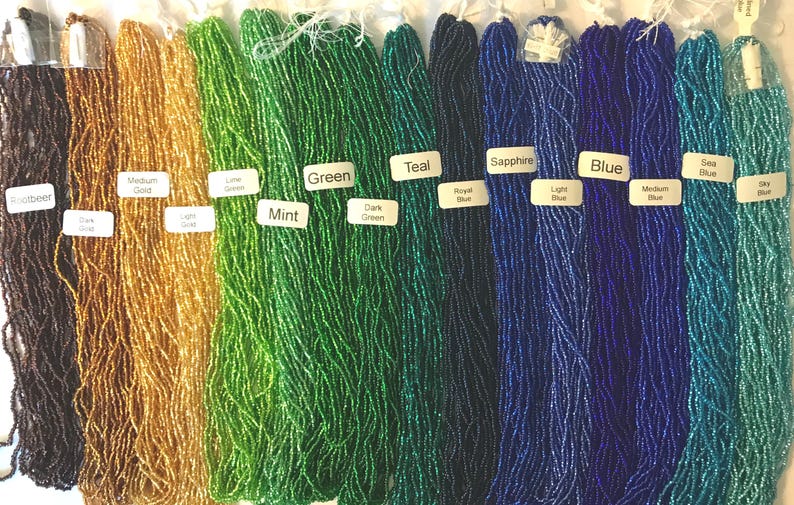 Puede incluir: Una variedad de cuentas de semillas en diferentes colores, incluyendo marr&oacute;n, dorado, verde, azul verdoso, zafiro, azul y azul marino. Las cuentas est&aacute;n dispuestas en filas, con cada fila representando un color diferente.