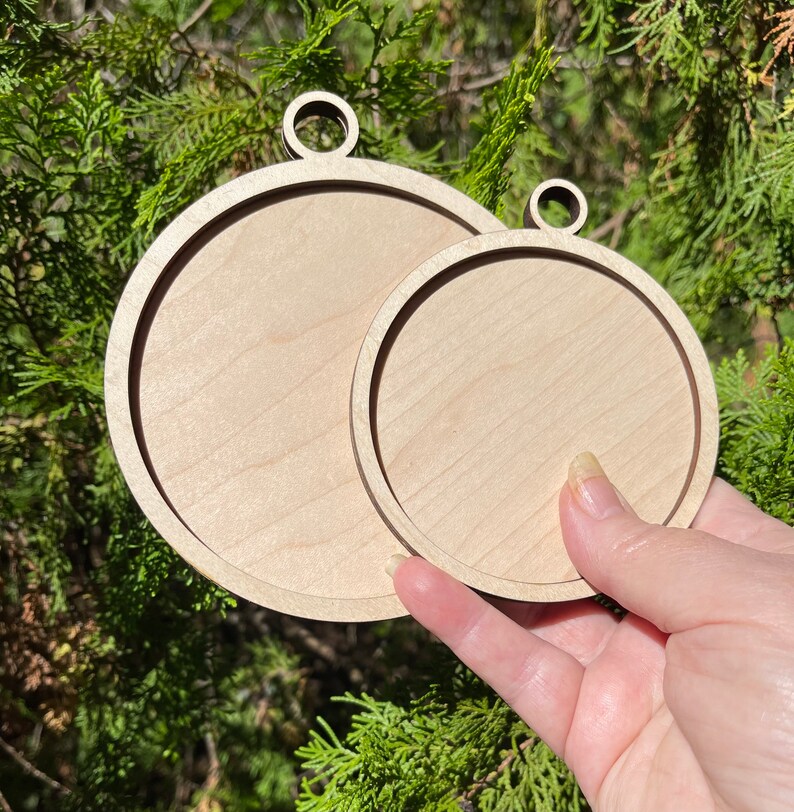 K&ouml;nnte beinhalten: Zwei unfertige runde Holzornamente mit einem Loch oben zum Aufh&auml;ngen. Das gr&ouml;&szlig;ere Ornament befindet sich hinter dem kleineren.