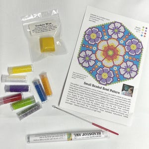 May include: A colorful beading kit for a small beaded bowl project. The kit includes a pattern, beads in eight colors, a needle, and a small block of wax. The pattern shows a flower design with a blue background.