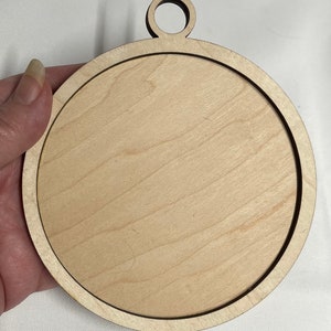 K&ouml;nnte beinhalten: Ein runder, unfertiger Holzanh&auml;nger mit einem Loch oben zum Aufh&auml;ngen. Der Anh&auml;nger ist aus hellem Holz gefertigt und hat eine glatte Oberfl&auml;che.