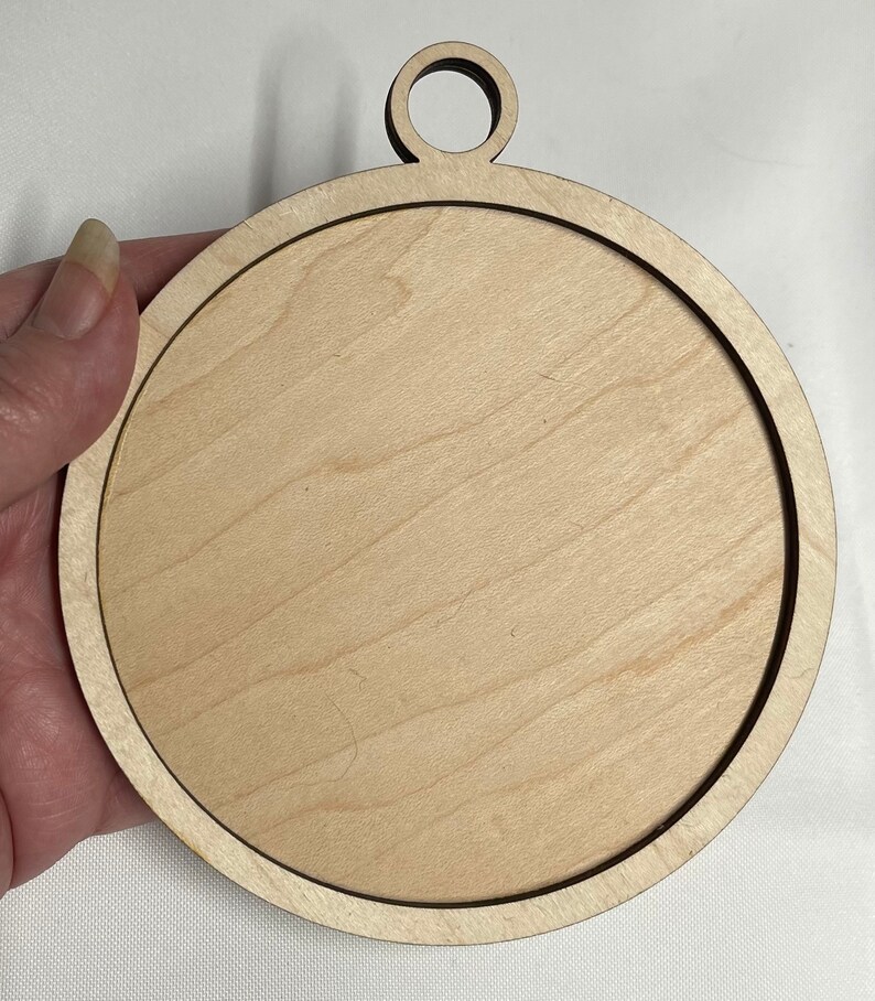 K&ouml;nnte beinhalten: Ein runder, unfertiger Holzanh&auml;nger mit einem Loch oben zum Aufh&auml;ngen. Der Anh&auml;nger ist aus hellem Holz gefertigt und hat eine glatte Oberfl&auml;che.