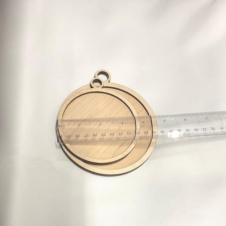 K&ouml;nnte beinhalten: Zwei unfertige Holzkreise mit einem Loch oben, der kleinere Kreis befindet sich innerhalb des gr&ouml;&szlig;eren Kreises. Die Kreise haben einen Durchmesser von 6,35 cm und 8,89 cm.