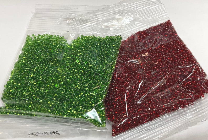 Puede incluir: Dos bolsas de cuentas de semillas, una verde y otra roja. Las bolsas son de pl&aacute;stico transparente y las cuentas son visibles.