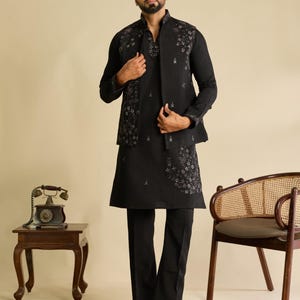 May include: A black long-sleeved kurta paired with matching black trousers and a sleeveless vest. The ensemble features intricate grey floral embroidery on the vest and the kurta hem. The vest has a high collar and the kurta has a V-neckline.