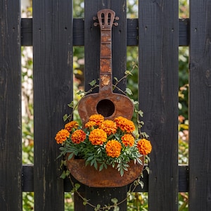 May include: A rustic, weathered metal wall planter shaped like an acoustic guitar. The brown, oxidized surface features a circular opening in the center. The planter is filled with vibrant orange marigold flowers and green foliage.
