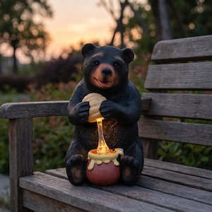 Könnte beinhalten: Eine schwarze Bärenfigur, die ein strukturiertes Wabenstück über einem kleinen braunen Honigtopf hält. Der Honigtopf verfügt über einen leuchtenden, beleuchteten Honigstrom, der mit der Wabe verbunden ist und einen warmen Lichteffekt erzeugt.