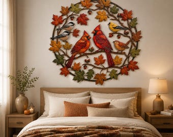 May include: A circular metal wall art piece featuring a wreath of autumn leaves in shades of red, orange, yellow, and green. The design includes two bright red cardinals, two small black and white birds, a yellow bird, and a brown bird perched on branches.