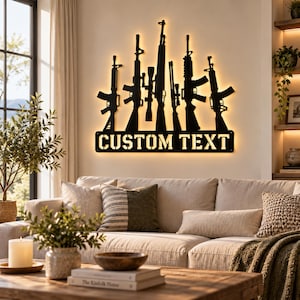 May include: A black metal wall art piece featuring silhouettes of five different rifles arranged in a row, backlit with warm LED lighting. Below the rifles is a rectangular panel with the cutout text CUSTOM TEXT in a bold, stencil-style font.