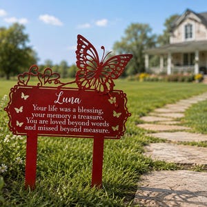 Könnte beinhalten: Ein roter Garten-Gedenkstecker aus Metall mit einem großen Schmetterlingsausschnitt an der Oberseite, Herzakzenten und dem Text: Luna, Your life was a blessing, your memory a treasure. You are loved beyond words and missed beyond measure. Kleine Schmetterlinge.