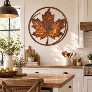 May include: A circular wall art piece featuring a large, detailed maple leaf design. The leaf is rendered in shades of copper, bronze, and rust, with a metallic finish. It is enclosed within a thin, circular metal frame that matches the leaf's tone.