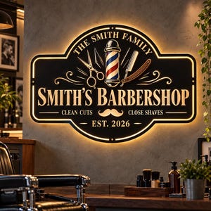 Peut inclure: Une enseigne murale noire rectangulaire aux coins arrondis avec rétroéclairage. Elle présente le texte "THE SMITH FAMILY", "SMITH'S BARBERSHOP", "CLEAN CUTS", "CLOSE SHAVES" et "EST. 2026", ainsi que des graphismes de poteau de barbier, ciseaux et rasoir.