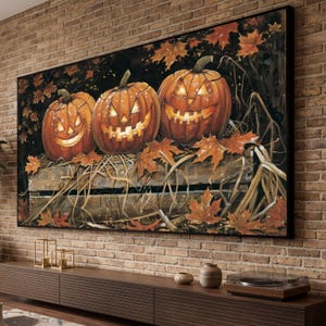 May include: A rectangular wall art print featuring three glowing jack-o'-lanterns resting on a wooden crate filled with straw and scattered orange maple leaves against a dark background, framed in a thin black border and mounted on a brick wall.
