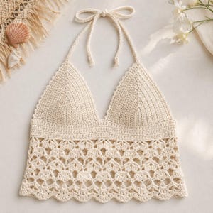 Può includere: Un top all'americana in uncinetto color crema con coppe triangolari a maglia fitta e una sezione inferiore caratterizzata da un intricato motivo traforato a smerlo. Il capo presenta sottili laccetti da annodare al collo e un orlo dritto.