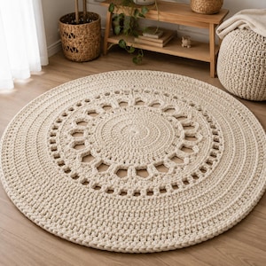 Puede incluir: Una alfombra redonda de ganchillo en color crema que presenta un disco central sólido rodeado por un patrón decorativo calado de bucles repetitivos, rematado con un borde ancho y texturizado de puntadas densas y uniformes.