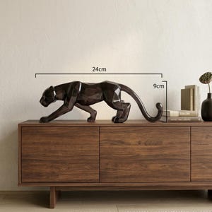 Op de afbeelding: Een donkerbruin, gefacetteerd geometrisch panterbeeld in een sluipende houding. Het beeld is 24 cm lang en 9 cm hoog, zoals aangegeven door de zichtbare meetlijnen en tekstlabels die boven het object worden weergegeven.