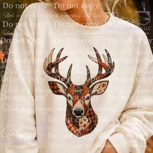 May include: A cream-coloured crewneck sweatshirt featuring a large graphic of a deer head. The deer is composed of various patterned sections, including red and black buffalo plaid, brown tones, and maple leaf prints, with prominent antlers.