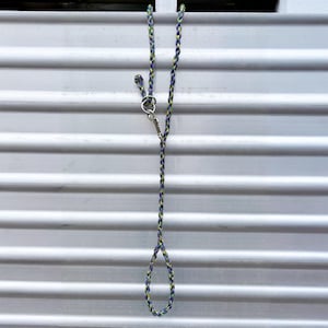 May include: A braided lead featuring a multi-coloured pattern of purple, blue, and lime green cord. The lead includes a silver-toned metal swivel snap hook attached to a ring, with a looped handle at the end for a secure grip during use.