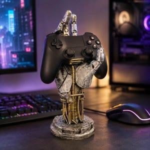 Può includere: Un controller per videogiochi nero appoggiato su un supporto a forma di mano robotica meccanica. La mano presenta una finitura argento invecchiato con ingranaggi e cavi dorati a vista, sostenuta da una base circolare con texture metallica.