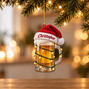 May include: A beer mug ornament featuring a red Santa hat with the name Christopher printed in red on the white brim. The mug is filled with golden beer, topped with white foam, and wrapped in a string of glowing yellow Christmas lights.