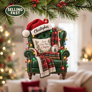Può includere: Un addobbo per albero di Natale a forma di poltrona verde trapuntata con un cappello da Babbo Natale rosso con la scritta Christopher. Include un cuscino con il testo Just One More Chapter, una tazza, libri, una coperta e luci natalizie.