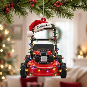 May include: A red lawn mower Christmas ornament featuring a black handle, a red Santa hat with the name Christopher printed in black script, and a string of multicoloured LED lights wrapped around the frame, hanging from a gold string.