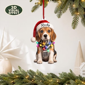 May include: A beagle puppy Christmas ornament hanging from a red ribbon. The puppy wears a red and white Santa hat with the name Rocky printed on the brim and a grey and white striped scarf wrapped with colourful miniature Christmas light bulbs.