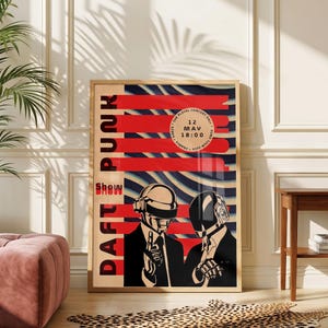 May include: A rectangular poster featuring the text DAFT PUNK and SHOW in a vertical red column. The artwork displays two figures wearing metallic helmets and suits against a background of blue and white wavy lines, with a circular event detail.