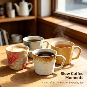 May include: Four ceramic mugs with angular handles, each featuring a unique textured finish in red, blue, white, and yellow, filled with hot coffee. The text "Slow Coffee Moments Handcrafted Ceramic for Everyday Joy" is printed in the corner.