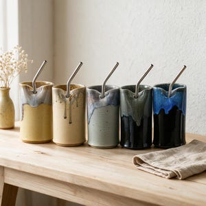 May include: Five cylindrical ceramic tumblers with a notched rim, each featuring a unique two-tone glaze with a drip effect. Each tumbler contains a bent stainless steel straw. The colors range from yellow and beige to green, grey, and black.