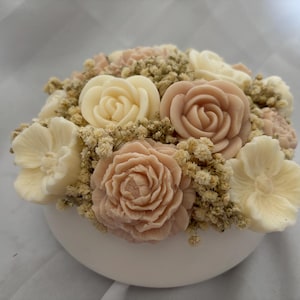 Op de afbeelding: Een ronde witte houder gevuld met een decoratief arrangement van crème en oudroze bloemvormen, afgewisseld met kleine trosjes gedroogde beige gipskruidbloemen, wat zorgt voor een dicht en gestructureerd botanisch geheel.