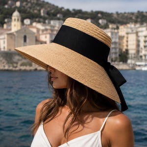 Peut inclure: Un chapeau de paille à larges bords avec une texture tissée beige naturel et une large bande en tissu noir entourant la calotte. La bande présente un nœud décoratif à l'arrière, créant un contraste avec la matière en paille beige clair.