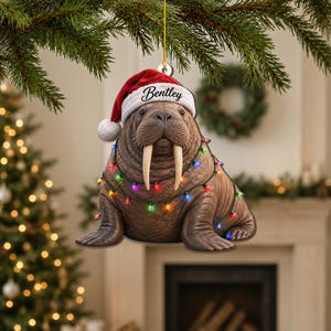 May include: A flat, hanging Christmas ornament shaped like a brown walrus with long tusks. The walrus wears a red and white Santa hat with the name Bentley printed on the brim and is wrapped in a string of colorful, glowing holiday lights.