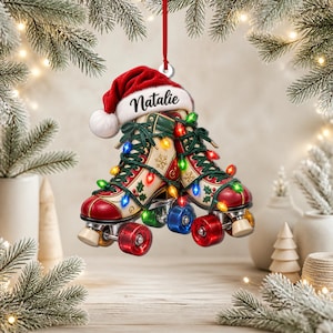 May include: A Christmas tree ornament featuring a pair of vintage-style roller skates decorated with holly patterns, wrapped in colorful string lights, and topped with a red Santa hat bearing the name Natalie in black script lettering.