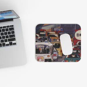 May include: A rectangular mouse pad featuring a detailed anime-style illustration of a busy city street filled with various cars and a bus. The artwork displays a dense traffic scene with multiple vehicles in shades of yellow, red, and blue, including a white bus with Japanese text and a circular sign with Japanese characters.