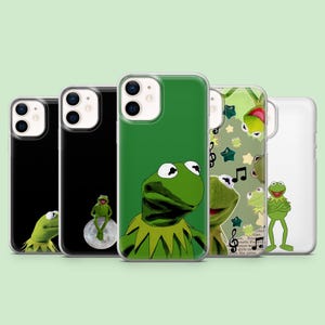 Könnte beinhalten: Eine Sammlung von fünf transparenten Smartphone-Hüllen mit verschiedenen Illustrationen einer grünen Froschfigur. Die Designs zeigen den Frosch auf dem Mond, ein Nahaufnahme-Porträt, eine Collage mit Musiknoten und Sternen sowie eine stehende Pose.