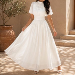 May include: A floor-length white dress featuring a high neckline, short flutter sleeves, and a fitted waistband. The bodice has vertical pleats, and the skirt is made of a flowing, lightweight fabric that extends to the floor in a full silhouette.
