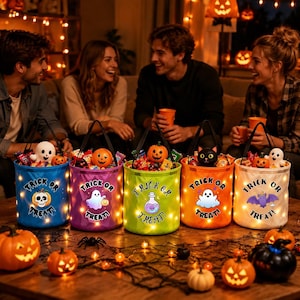 May include: Five cylindrical Halloween candy buckets with LED lights, each featuring a unique graphic like a ghost, skull, or bat, and the text Trick or Treat. The buckets are filled with assorted sweets and sit on a wooden surface.