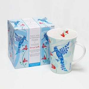 Peut inclure: Un mug en céramique blanche et sa boîte assortie ornés d'un motif de colibri bleu avec des accents floraux rouges. La boîte affiche le texte Peace, Love & Happiness, Paix, Amour et Bonheur, et la signature de l'artiste Francis Dick en rouge.