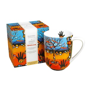 May include: A ceramic mug and its matching square box featuring a vibrant design of a tree against a blue sky, orange ground, and black hand silhouettes. The text on the box reads REMEMBER SOUVIENS-TOI by Rombough, with additional descriptive text.