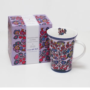 Peut inclure: Un mug en porcelaine et sa boîte carrée assortie, tous deux décorés d'un motif floral boisé coloré avec des oiseaux et des plantes stylisés rouges, bleus et violets. La boîte porte le texte Woodland Floral, Bouquet des Bois et Norval Morrisseau.